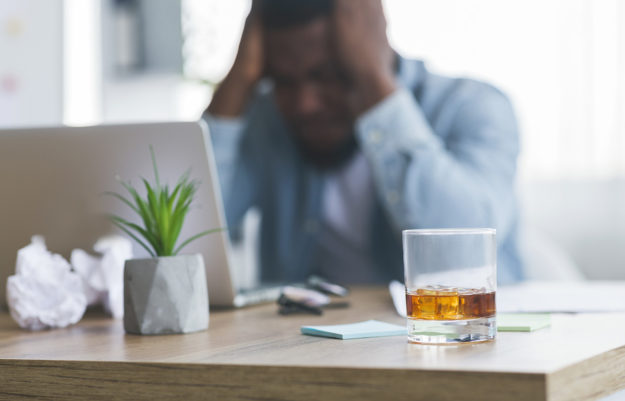 A man holds his head as he struggles with recognizing alcoholism signs