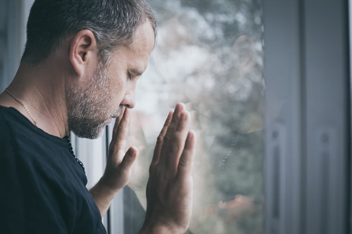 man looking out window considering common addiction triggers