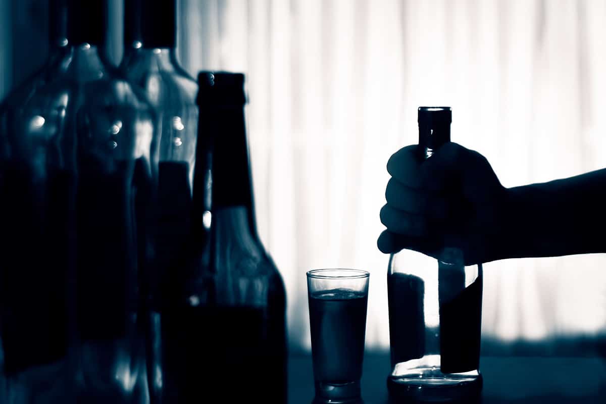silhouetted hand reaching for liquor bottles showing what is binge drinking