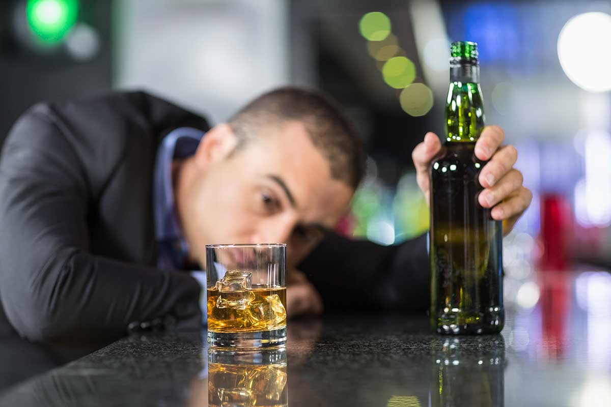 man at bar with bottle and glass of alcohol showing alcohol dependence