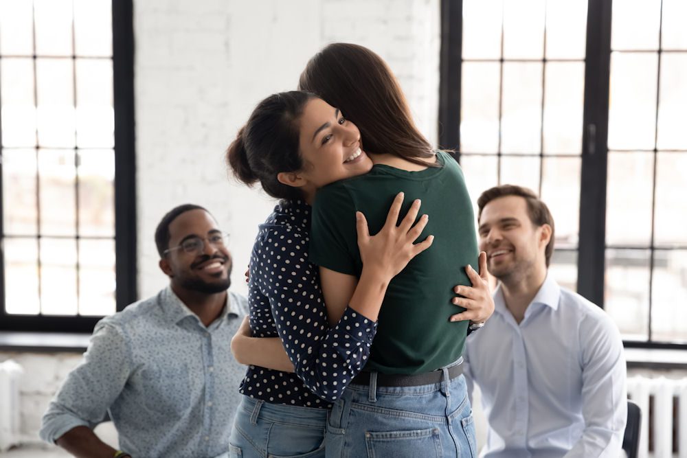 Support group members embracing during a recovery meeting following a cocaine addiction intervention.