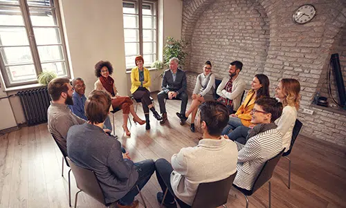 a group of people sit in chairs in a circle during a 12 step program